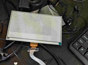 a e-ink screen loose on a desk, covered in garbage